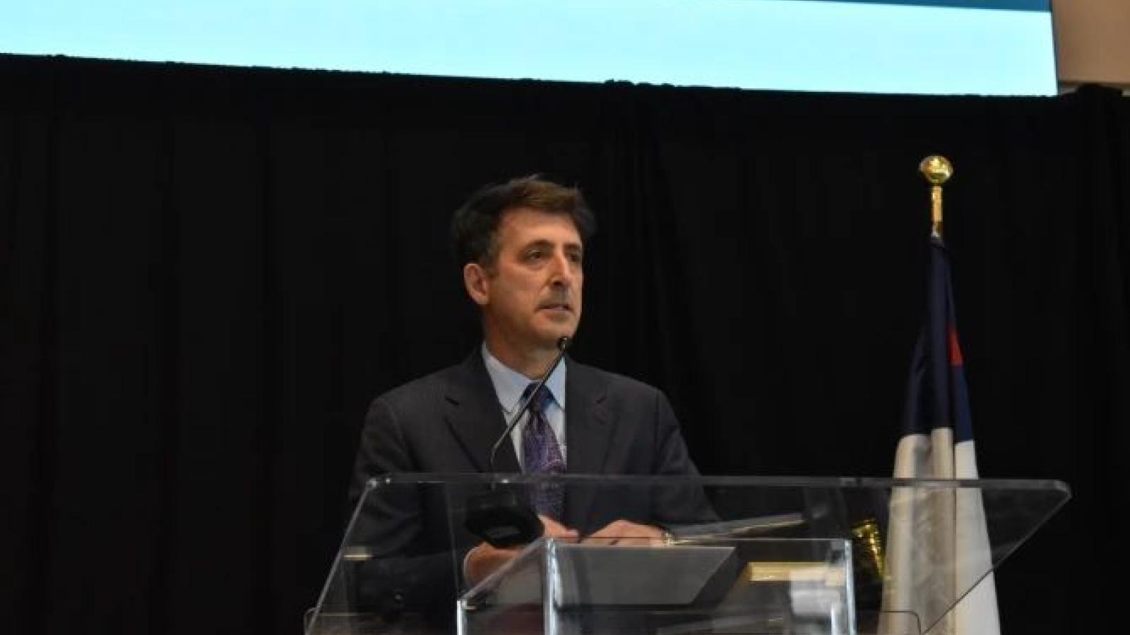 Dr. Andrew Abela speaking at a podium. 