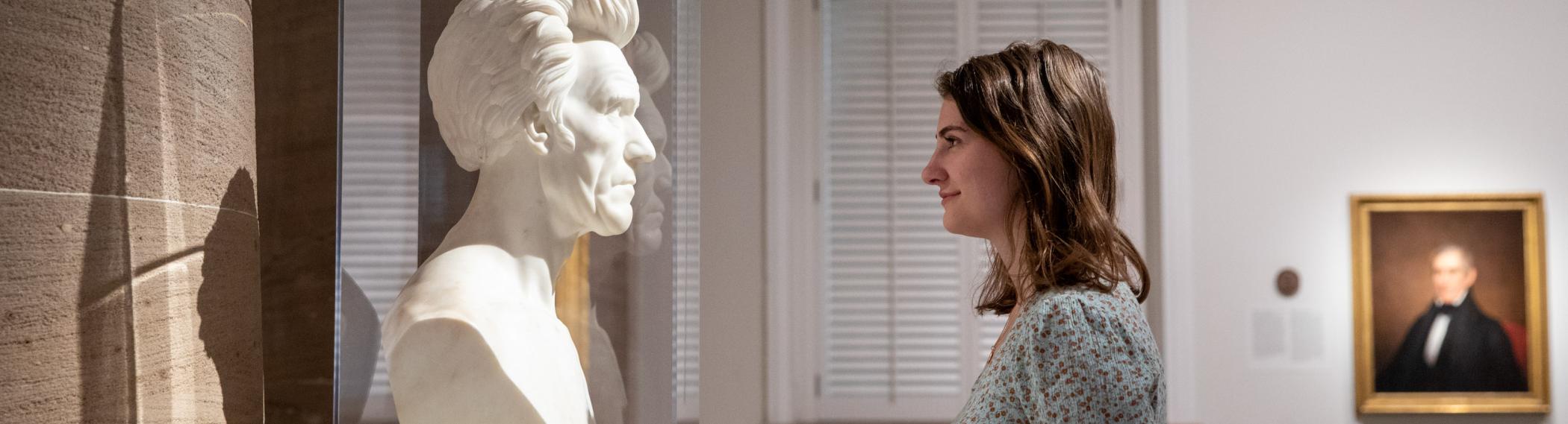 young woman staring eye to eye of a statue of Lincoln in a museum