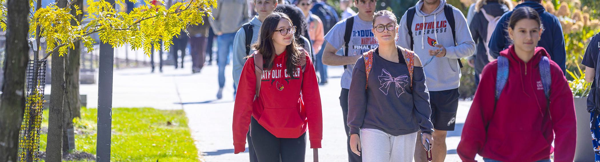 Crowd of students walking on campus sidewalk.