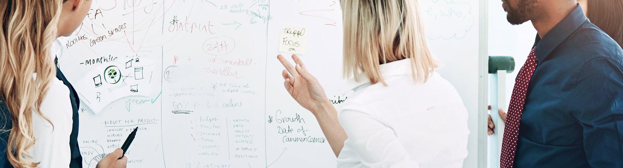 Photo of workers at a white board, working on a problem.