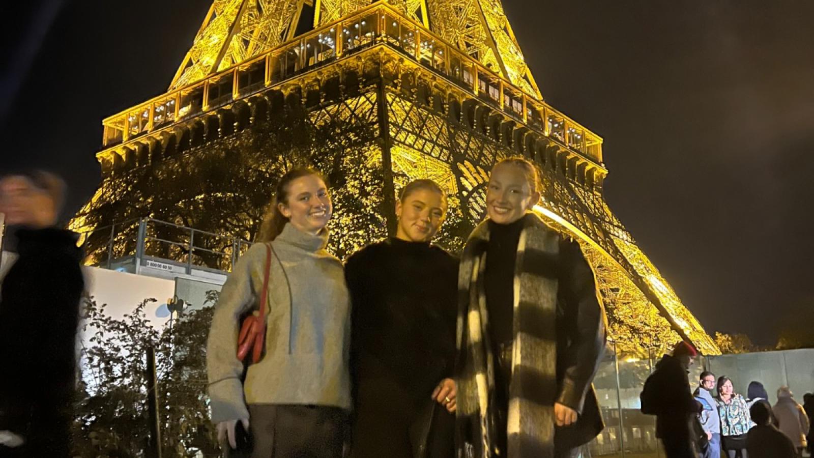 cate and 2 friends at the base of the eiffel tower at night