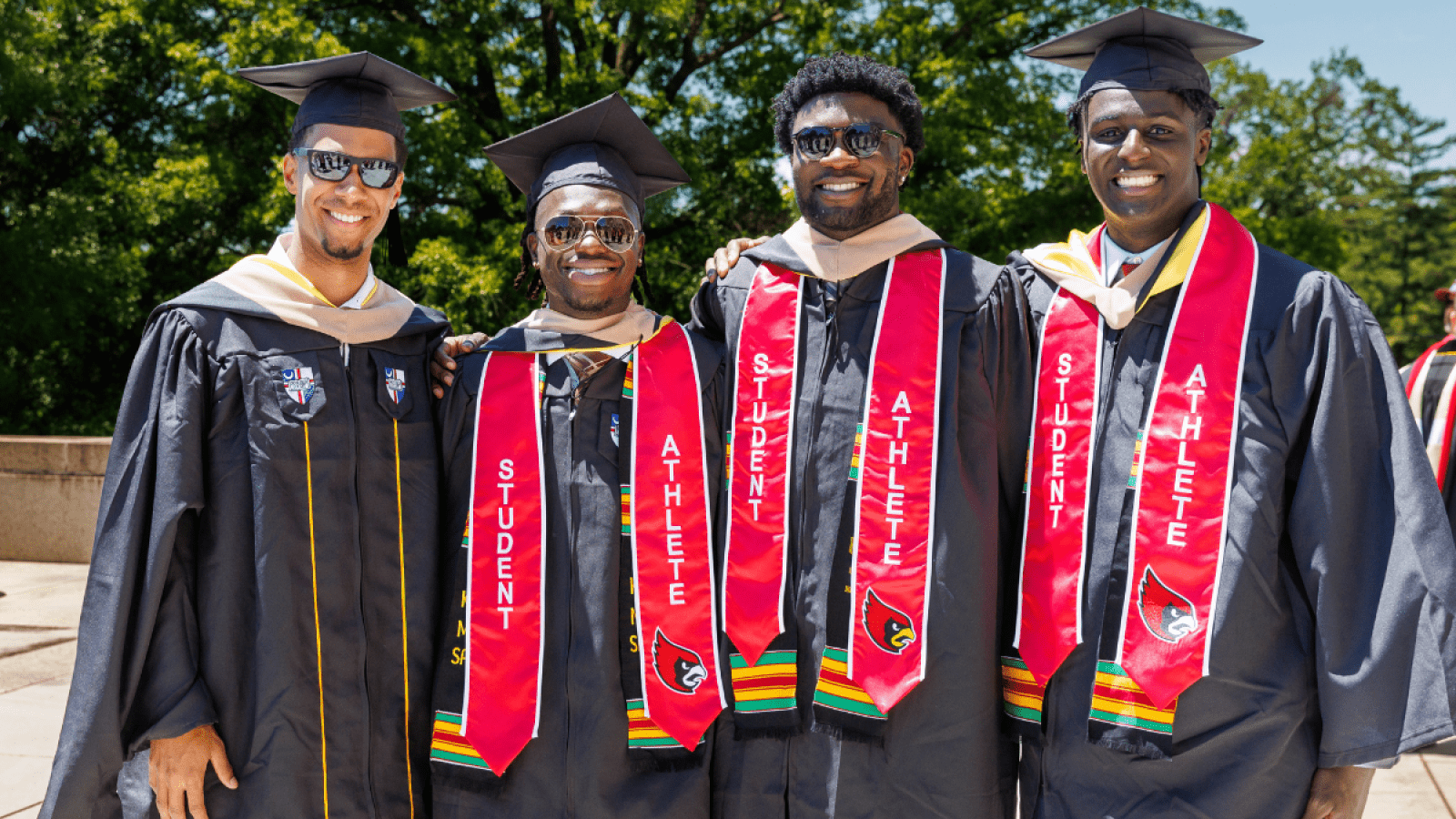 Four students in their regalia for Commencement, smiling at the camera.