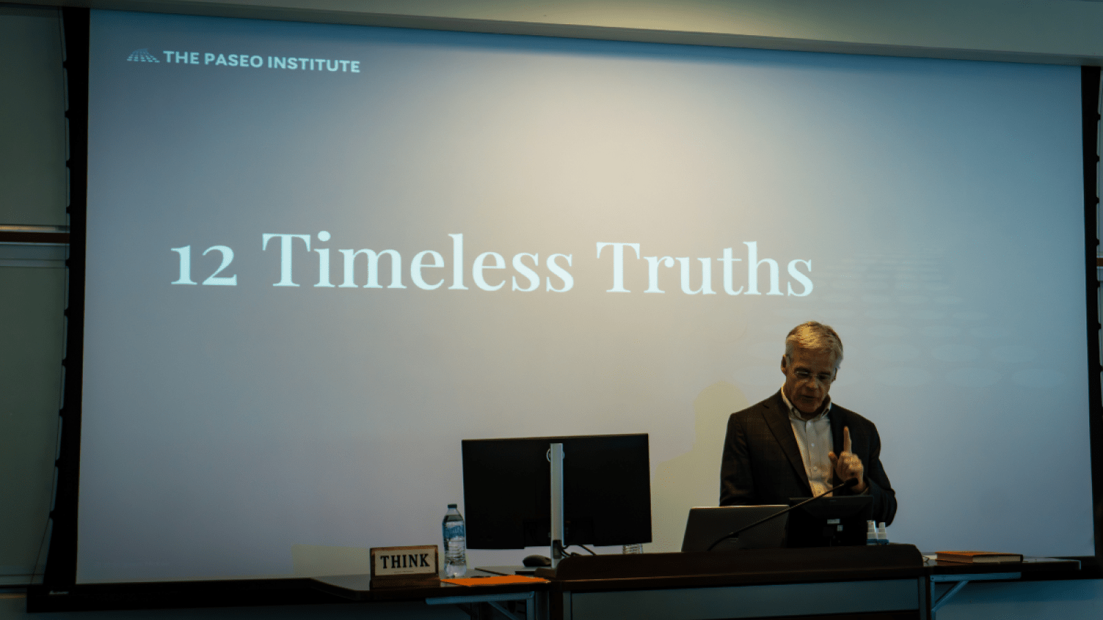 Steve McKee is delivering a lecture in front of a screen that says "12 Timeless Truths."