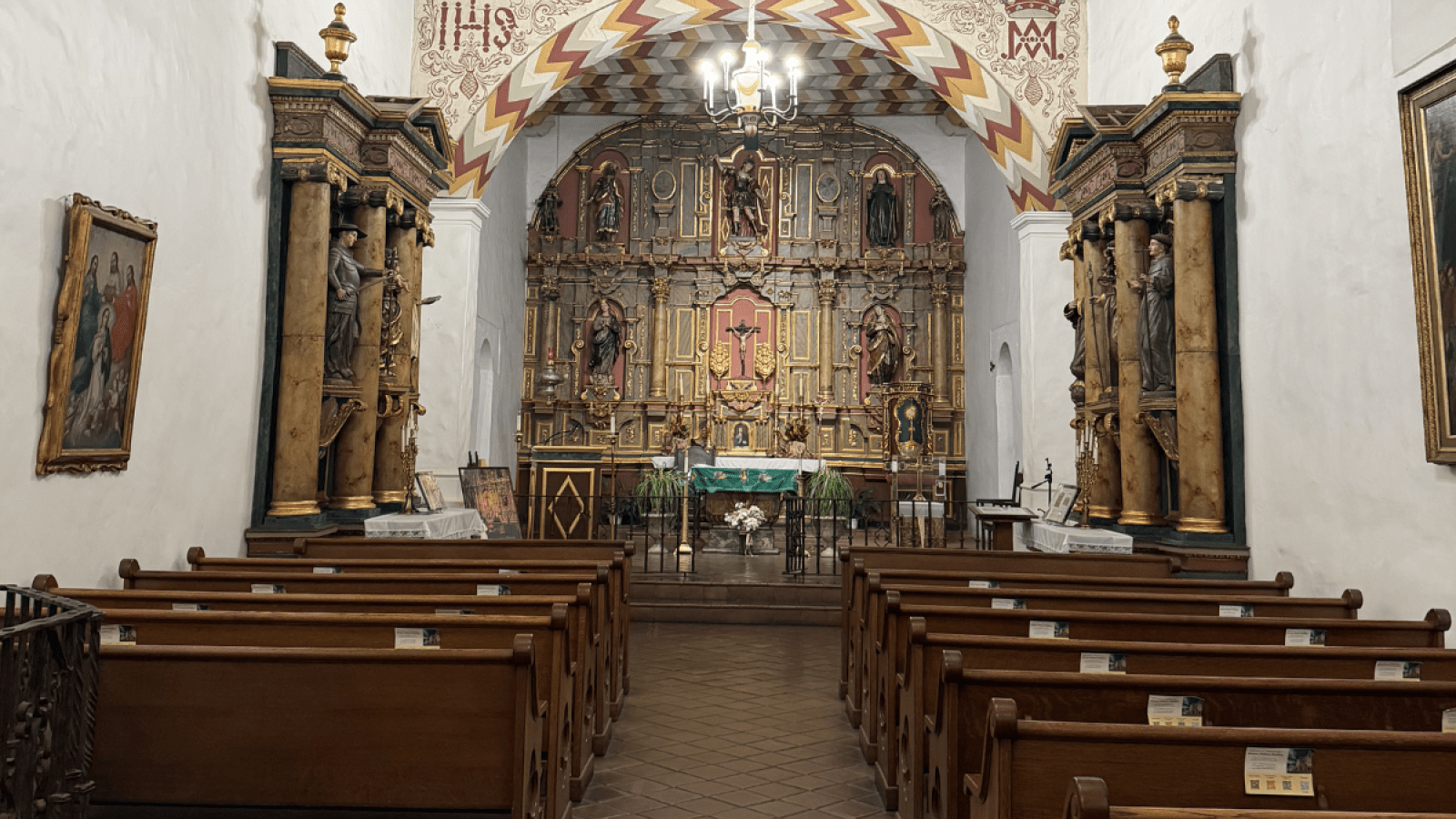 Mission Dolores Basilica in San Francisco, California. It is a small, white church with a red and gold ceiling and altar. Wooden pews line both walls.