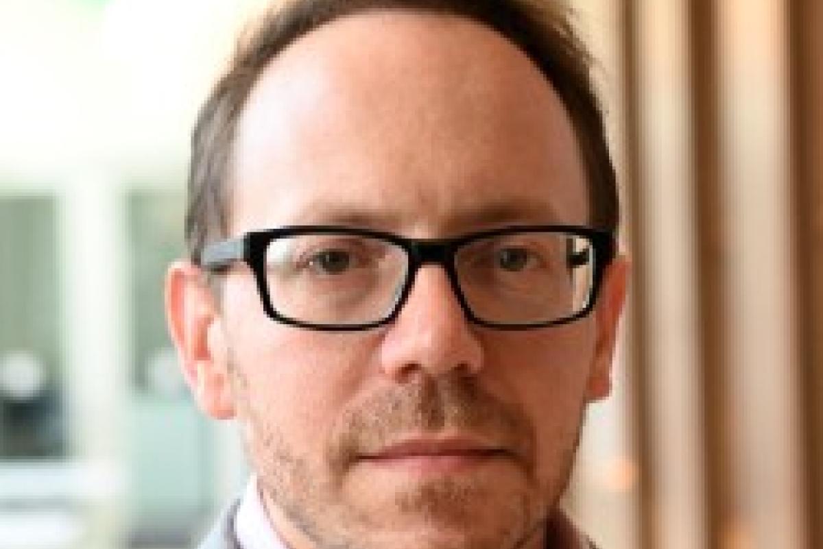 Photo of Anthony P. Cannizzaro. He has short brown hair, thick black glasses, and is wearing a grey shirt over a pink shirt.