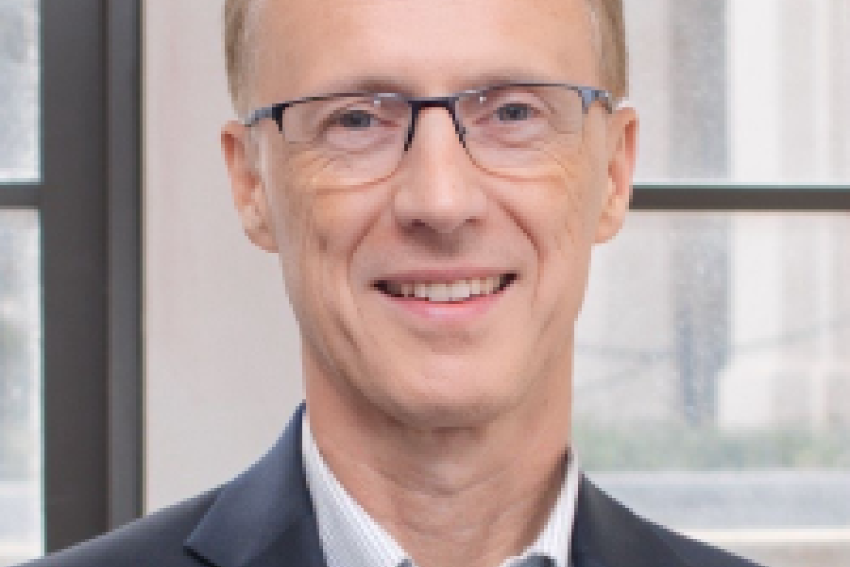 Photo of John Egan. He has short light brown hair, thin glasses, and is wearing a light blue shirt under a navy blazer.