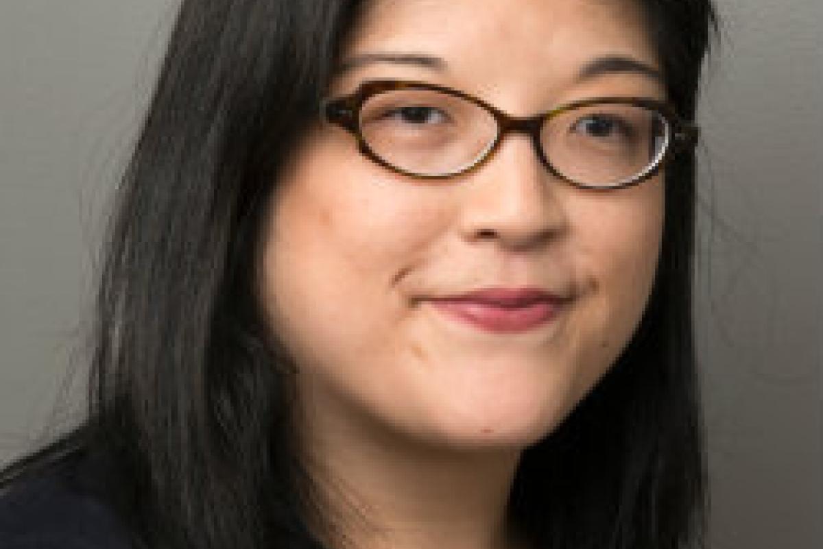 Photo of Irene Kim. She has should-length black hair. She has cat-eye glasses and is wearing a black and yellow blouse.