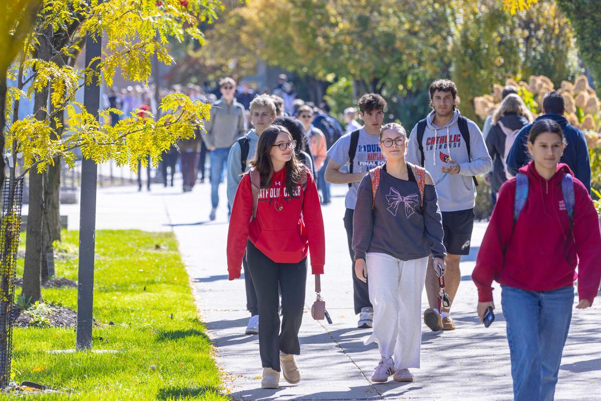 Crowd of students walking on campus sidewalk.