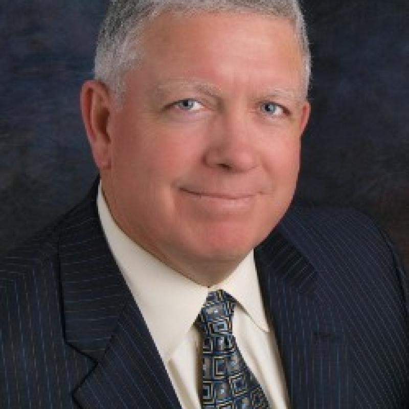 Photo of Robert J. Scanlon. He has grey hair and is wearing a navy suit with a white shirt and green tie.