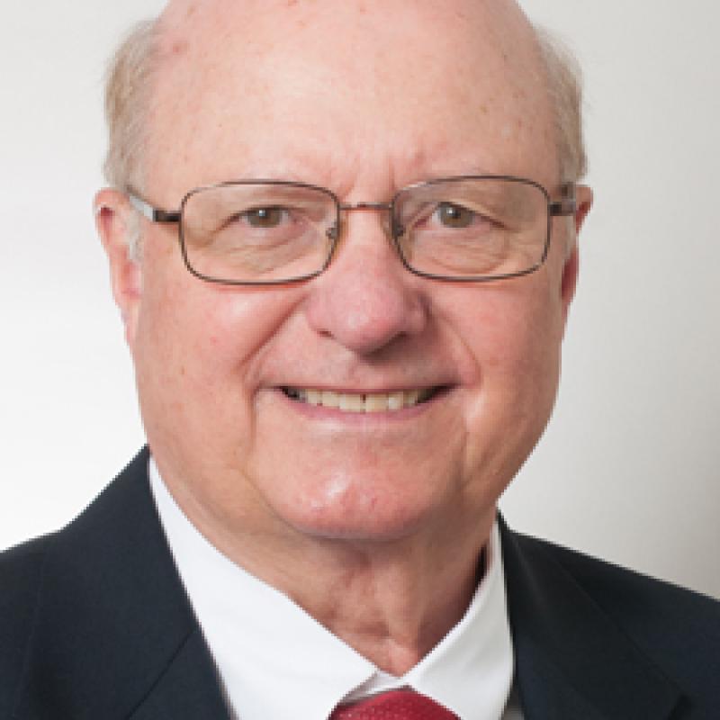 Photo of Raymond Wyrsch. He has thin glasses. He is wearing a black suit jacket and a white shirt and a red tie.