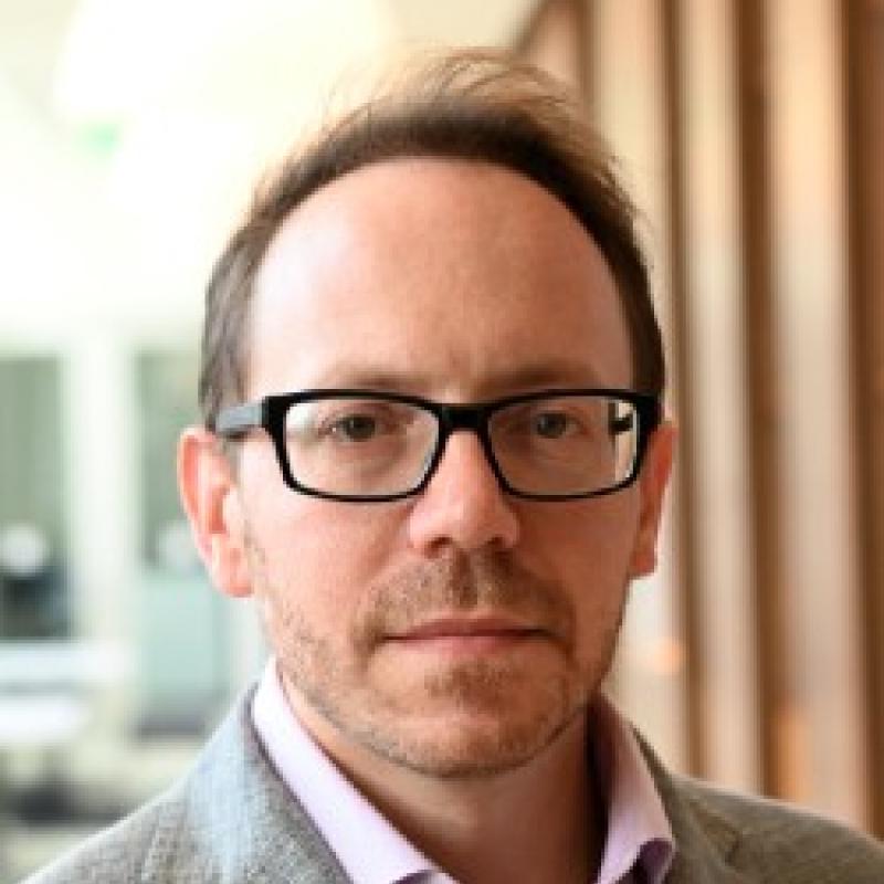 Photo of Anthony P. Cannizzaro. He has short brown hair, thick black glasses, and is wearing a grey shirt over a pink shirt.