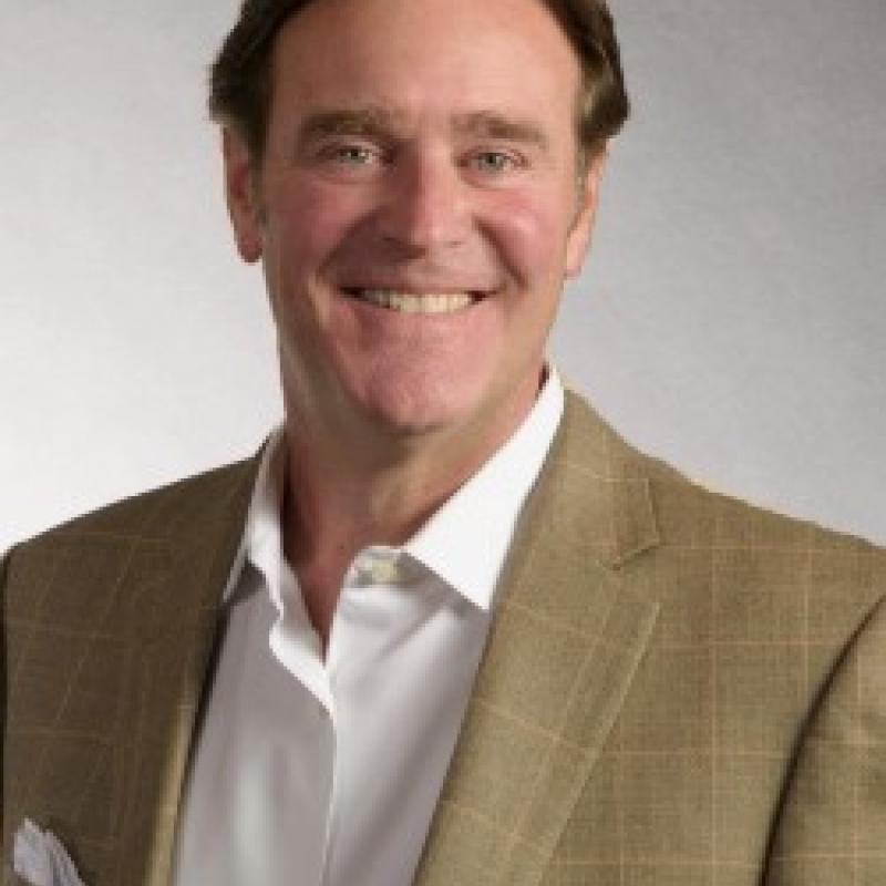 Photo of Doug Traxler. He has short brown hair. He is wearing a brown checked suit jacket over a white shirt.