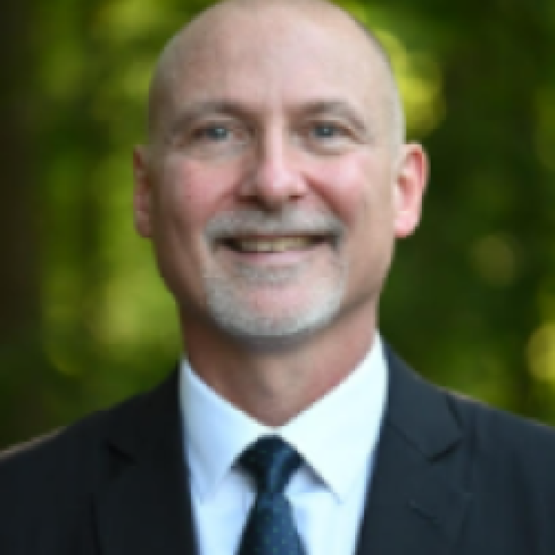 Photo of Gregory Monahan. He is wearing a black suit, a white shirt, and a navy tie.