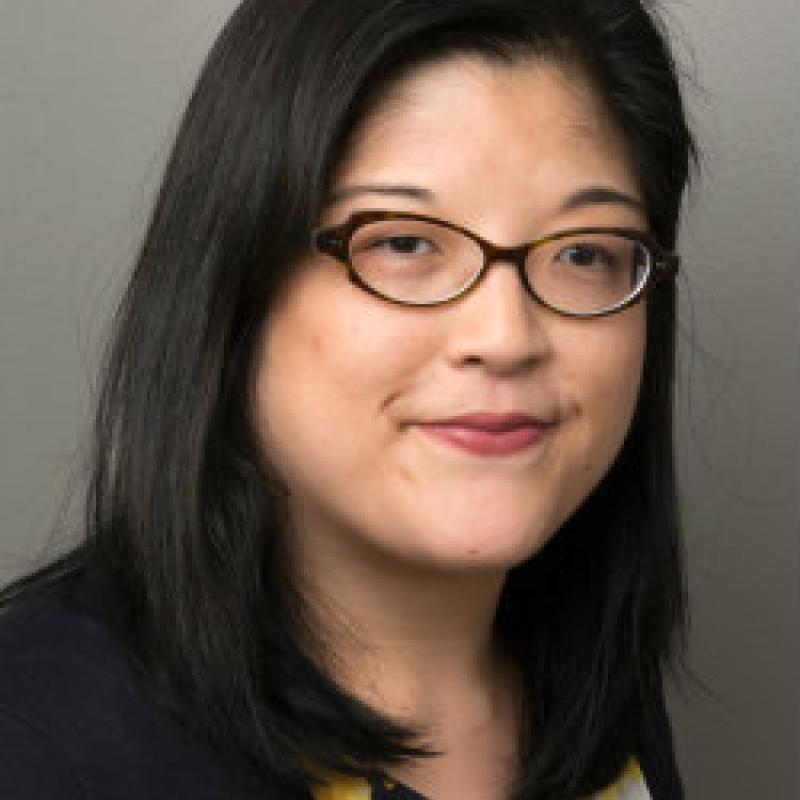 Photo of Irene Kim. She has should-length black hair. She has cat-eye glasses and is wearing a black and yellow blouse.