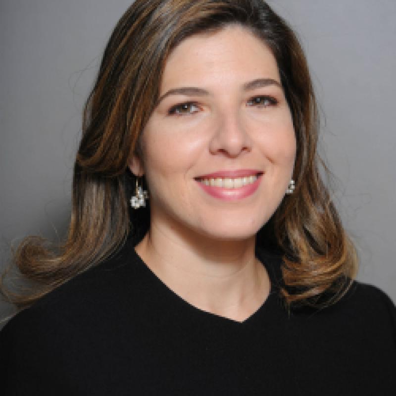 Photo of Beatriz Lopez Bonetti. She has brown hair. She is wearing a black shirt and is against a grey background.