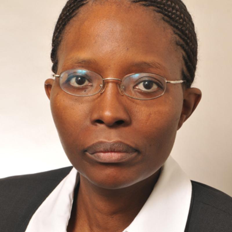 Photo of Mary M Njeri Njai. She is wearing a black suit with a white shirt and is wearing thin glasses.