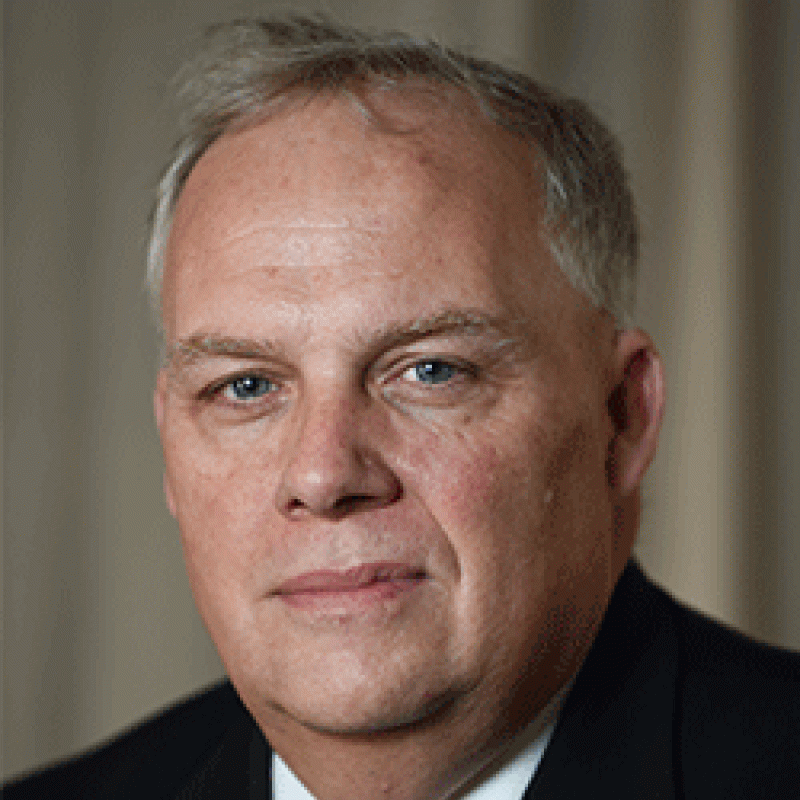 Photo of Robert Nugent. He is wearing a black suit and a white shirt with a red tie.