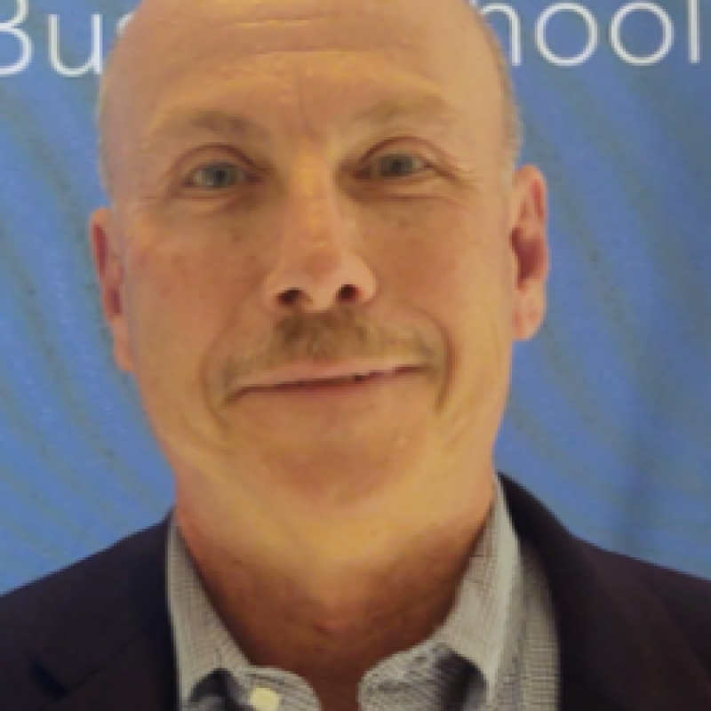 Photo of John O'Hare. He is wearing a black suit and a blue shirt. He has a light mustache.