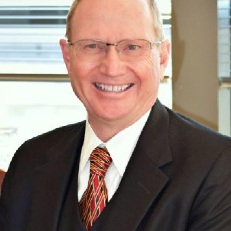 Photo of J Patrick Kearns. He is wearing a black suit and a red, green, and blue tie.