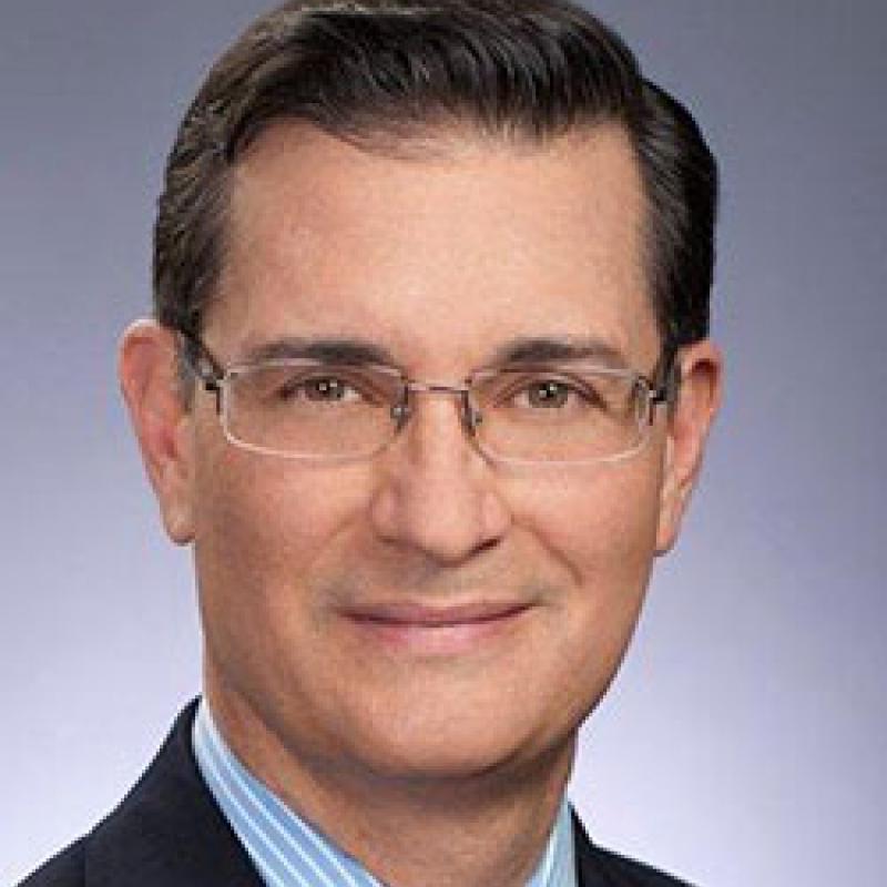 Photo of Peter Pin. He has short dark hair and thin glasses. He is wearing a dark suit and a blue striped shirt with a yellow tie.