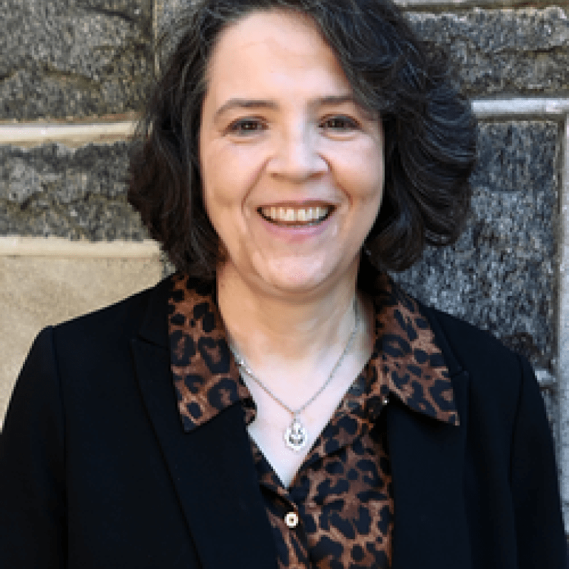 Photo of Rebecca Ryskind Teti. She has bobbed dark hair. She is wearing a black cardigan over an animal print button down shirt.
