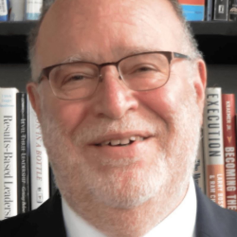 Photo of Max Torres. He wears thin glasses as well as a black suit, a white shirt, and a red tie.
