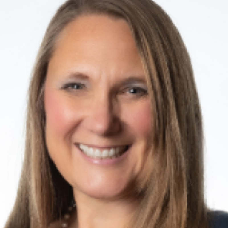 Photo of Tracy Phillips. She has long blonde-brown hair and is wearing  a black blouse with a string of pearls.