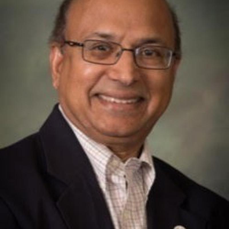 Photo of Julian Gaspar. He has short grey hair and thin glasses. He is wearing a black suit over a checked shirt.