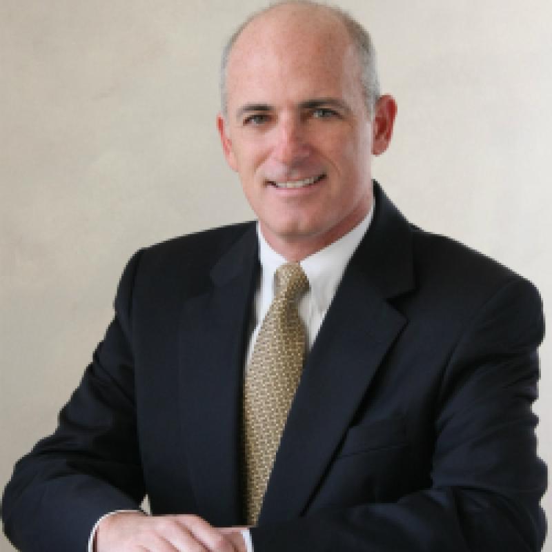 Photo of Mark Weber. He is wearing a black suit, a white shirt, and a gold tie.