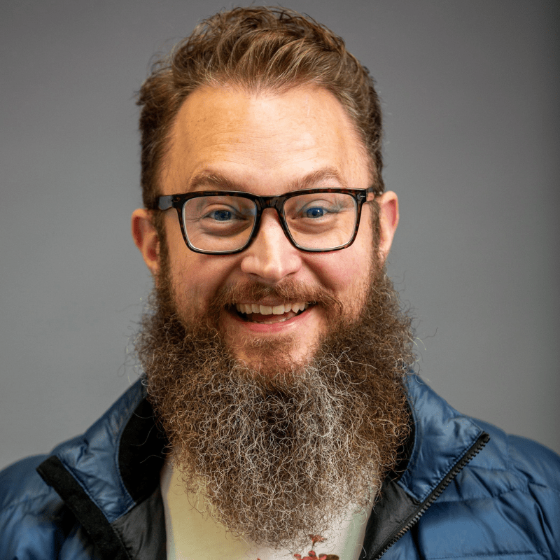 Photo of Taylor Black. He has a long salt and pepper beard and thick frame glasses. He is wearing a blue puff jacket and a tshirt.