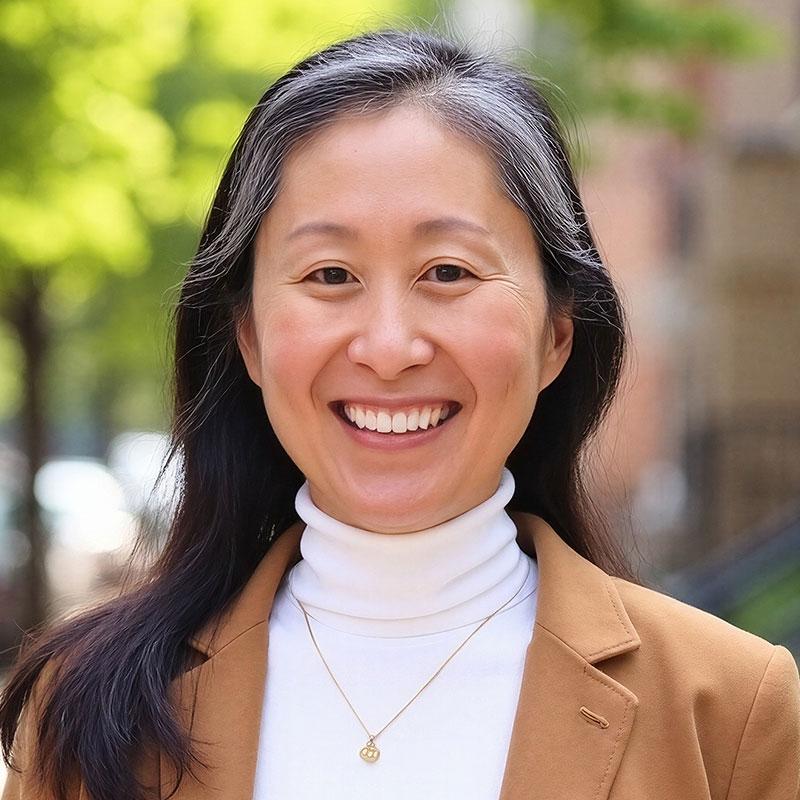 Photo of Cabrini Pak. She has long black hair and is wearing a tan professional jacket.