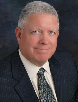 Photo of Robert J. Scanlon. He has grey hair and is wearing a navy suit with a white shirt and green tie.
