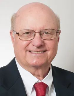 Photo of Raymond Wyrsch. He has thin glasses. He is wearing a black suit jacket and a white shirt and a red tie.