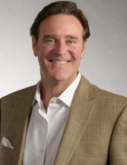 Photo of Doug Traxler. He has short brown hair. He is wearing a brown checked suit jacket over a white shirt.