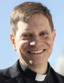Photo of Robert Gahl. He has short brown hair and is wearing a black shirt and a clerical collar.