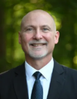 Photo of Gregory Monahan. He is wearing a black suit, a white shirt, and a navy tie.