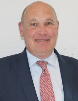Photo of Frank Kelly. He is wearing a navy suit over a light blue shirt with a red and white tie.