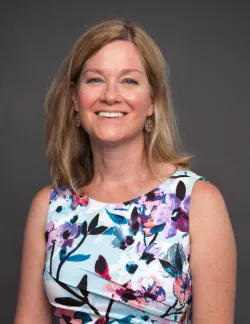Photo of Jeanne Mancini. She has shoulder-length blonde hair and is wearing a floral dress.