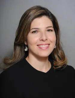 Photo of Beatriz Lopez Bonetti. She has brown hair. She is wearing a black shirt and is against a grey background.