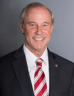 Photo of Stewart McHie. He is wearing a black suit, a white shirt, and a red and white tie. He has short grey hair.