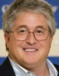 Photo of Michael Troilo. He is wearing thin glasses and has grey hair. He is wearing a navy suit jacket over a blue striped shirt.