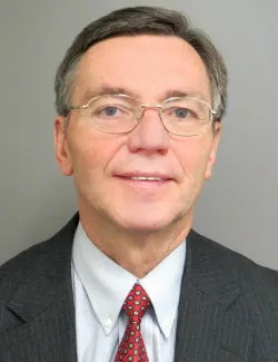 Photo of Mark Michalski. He is wearing a grey suit with a white shirt and a red spotted tie. He has short grey hair and white glasses.