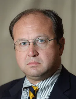 Photo of Michael New. He is wearing a navy suit, a striped shirt, and a yellow and black tie.