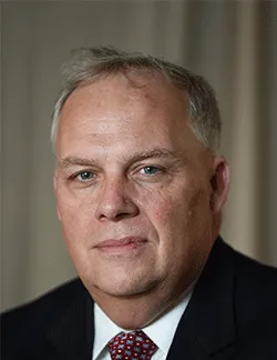 Photo of Robert Nugent. He is wearing a black suit and a white shirt with a red tie.