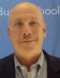 Photo of John O'Hare. He is wearing a black suit and a blue shirt. He has a light mustache.