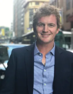 Photo of Patrick Langrell. He has curly blonde hair. He is wearing a navy blazer and a blue shirt.