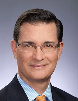 Photo of Peter Pin. He has short dark hair and thin glasses. He is wearing a dark suit and a blue striped shirt with a yellow tie.