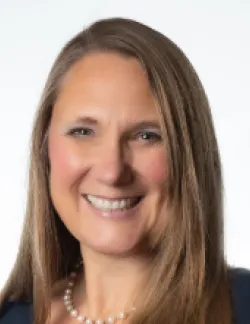 Photo of Tracy Phillips. She has long blonde-brown hair and is wearing  a black blouse with a string of pearls.