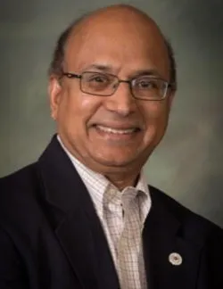 Photo of Julian Gaspar. He has short grey hair and thin glasses. He is wearing a black suit over a checked shirt.