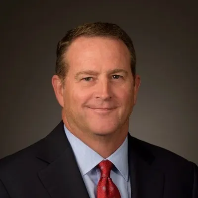Photo of Michael Greaney. He is wearing a black suit jacket over a light blue shirt and a red tie.